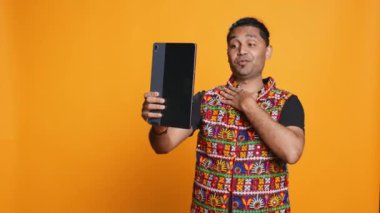 Çevrimiçi video görüşmesinde arkadaşını selamlayan ışıltılı adam, dostça jestler yapıyor. Telekonferansta arkadaş ile iletişim kuran neşeli kişi tablet, stüdyo arka planı, kamera B