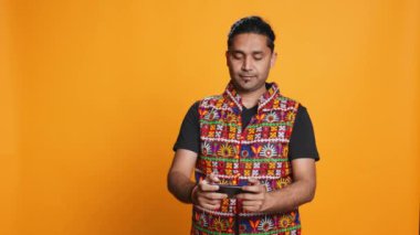 Hintli bir adam cep telefonuyla oyun oynuyor peyzaj modunda, boş zamanların tadını çıkarıyor. Oyuncu cep telefonundan zevk alıyor, eğleniyor, stüdyo arka planında izole edilmiş, kamera B