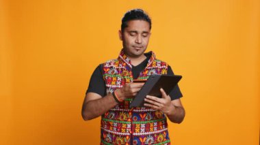 Adam alışveriş sitesine tablet kullanarak ödeme metodu ekliyor, promosyonlardan faydalanıyor, stüdyo geçmişi kullanıyor. Hintli kişi internetten bir şeyler alıyor, kredi kartı kullanıyor, cihaz üzerinde veri yazıyor, kamera B