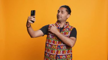 Hintli narsist adam her açıdan selfie çekmek için cep telefonu kullanıyor. Sosyal medya kullanıcısı telefon kamerasıyla fotoğraf çekiyor, mutlu bir şekilde gülümsüyor, stüdyo arka planı, kamera B