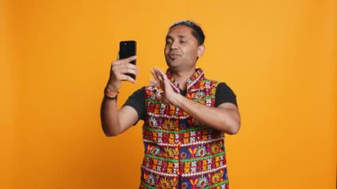 Mutlu bir adam, arkadaşlarıyla internet üzerinden telefon görüşmesi yapıyor, dostça jestler yapıyor. Telekonferansta arkadaşınla iletişim kurarken gülümseyen kişi cep telefonu, stüdyo arka planı, kamera B