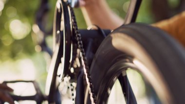 Close-up shot of two persons greasing chain of modern bicycle in home yard. Detailed view of caucasian boyfriend applying grease to bike components with the help african american girlfriend outdoor. clipart