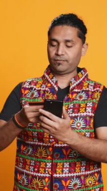 Dikey videolu Hintli adam cep telefonu web sitesine ödeme metodu ekliyor, bir şeyler satın alıyor, stüdyo arka planında izole edilmiş. Müşteri internet alışverişi yapıyor, cep telefonu ve kamera B 'de banka kartı bilgileri yazıyor.