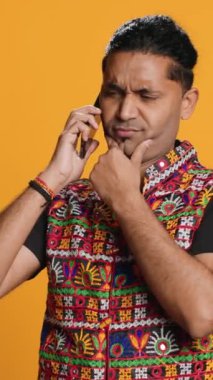 Dikey görüntülü Hintli adam akıllı telefondan en iyi arkadaşıyla konuşuyor. Neşeli insan telefonda arkadaşıyla konuşuyor. Cep telefonu kullanıyor. Stüdyo arka planında izole edilmiş.