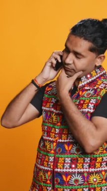 Dikey görüntülü Hintli adam akıllı telefondan en iyi arkadaşıyla konuşuyor. Neşeli insan telefonda arkadaşıyla konuşuyor cep telefonu kullanıyor, stüdyo arka planında izole edilmiş, kamera B