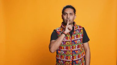 Otoriter adam el kol hareketi yapıyor, gizlilik talep ediyor, gürültüden rahatsız oluyor. Sert adam şikâyet ediyor, parmağını dudaklara koyuyor, sessiz uyarı işareti hareketi yapıyor, stüdyo arka planı, kamera B