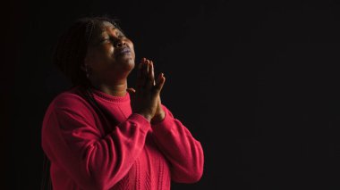 Graceful black woman gazing upwards with palms extended in gesture of reverance and adoration. Side-view portrait of african american lady engaged in prayerful reflection in isolated background. clipart