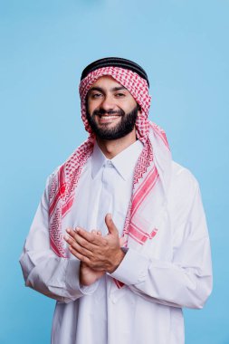 Geleneksel cüppeli, güler yüzlü Müslüman adam elleriyle alkışlıyor ve sunumda destek veriyor. Neşeli genç Arap alkış hareketi yapıyor ve kameraya bakıyor.
