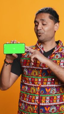 Geleneksel giysiler içinde dikey video içeriği yaratıcısı izole edilmiş ekranlı telefon ve stüdyo arkaplanı öneriyor. Hintli adam internetteki teknoloji kanalı, kamera B için kopyalama alanı modelleme akıllı telefon cihazını inceliyor.