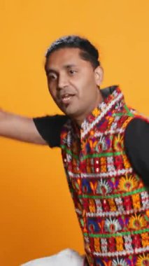 Dikey video yıldızı eğleniyor, oryantal müzik eşliğinde dans ediyor, dinlenme zamanının tadını çıkarıyor. Neşeli adam Bollywood dans hareketleri yapıyor, stüdyo arka planında izole edilmiş, kamera B