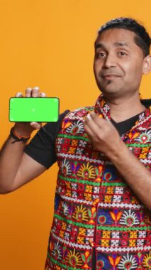 Yeşil ekran cep telefonunu sunan dikey video içerik yaratıcısı, stüdyo arka planında izole edilmiş. Hintli kişi internet kanalı için kopya alanı modelleme akıllı telefon aygıtı, kamera B 'yi inceliyor