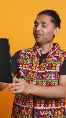 Dikey video rahatlamış adam, arkadaşlarıyla internetten görüntülü konuşma yaparken eğleniyor. Kaygısız Hintli arkadaşla telekonferansta tartışıyor. Tablet, stüdyo arka planı kullanarak.