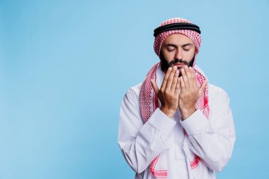 Geleneksel giysiler giymiş Müslüman bir adam dua ederken avuç içi açık duruyor. Tanrı 'dan lütuf dilerken, başörtüsü ve başörtüsüyle dindar Arap duası.