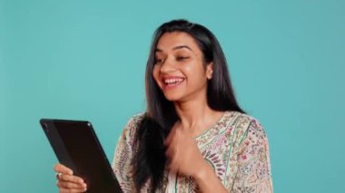 Neşeli bir kadın video konferans sırasında arkadaşlarıyla dedikodu yapıyor. Tablet kullanıyor, stüdyo geçmişi kullanıyor. Neşeli insan arkadaşlarıyla bağ kuruyor, internetteki video görüşmesi sırasında söylentiler yayıyor, kamera B