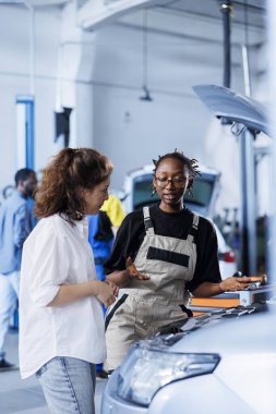 Araba tamirhanesinde araba tamircisine yardım eden eğitimli bir tamirci. Garajda çalışan biri, hasarlı araç yakıt deposunu tamir ediyor.