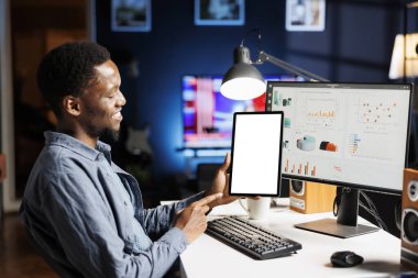 Boş ekranla tablet üzerinde çalışan genç, bilgisayardaki muhasebe istatistiklerini değerlendirmeden önce çalışma yerinde oturuyor. Beyaz ekran şablonlu Afrika kökenli Amerikalı adam tutma aygıtı.