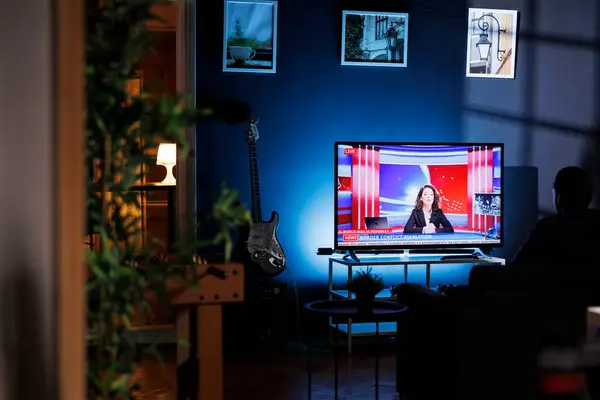 stock image Relaxed person watching breaking news on television at night, chilling on sofa in living room and watching tv program. Young adult listening to media information on global network.