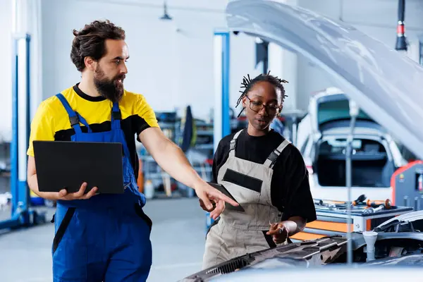 stock image Technician servicing broken vehicle, checking for faulty brakes under manager supervision. Smiling repairmen in auto repair shop working together on fixing automobile, discussing best options