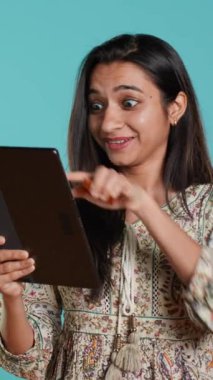 Dikey videolu neşeli kadın ürünleri satın almak için heyecanlanıyor, web sitesine ödeme metodu ekliyor, stüdyo arka planında soyutlanıyor. Mutlu müşteri internet alışverişi yapıyor, tablet üzerinde banka kartı bilgileri yazıyor