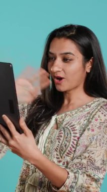 Telekonferans toplantısında tablet ve stüdyo arkaplanı kullanarak dostça sohbet eden dikey videolu bir kadın. Çevrimiçi video görüşmesi sırasında arkadaşlarla sohbet eden kişi