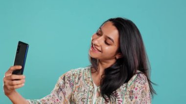 Selfie 'ye gülümseyen neşeli Hintli kadın onları cep telefonuyla sosyal medyaya yüklüyor. Neşeli kız fotoğraf çekiyor. Fotoğraf makinesi kullanıyor. Stüdyo arka planında izole edilmiş.