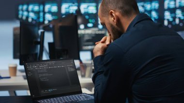 Bilgisayar bilimci veri merkezi sunucularını denetliyor, dizüstü bilgisayarda kod yazıyor, sorun yaratıyor. Yazılım uzmanı ana bilgisayarlarda bakım yapıyor. Not defteri kullanıyor, yakın çekim yapıyor.