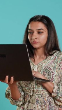 Dikey videolu Hintli kadın dizüstü bilgisayarda yazı yazıyor ve küfür ediyor, işine kızıyor. Not defterine e-posta yazan, yüksek sesle şikayet eden, stüdyo arka planında izole edilmiş, kamera A