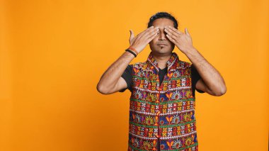 Man wearing traditional indian clothing covering eyes, ears and mouth, imitating three wise monkeys, doing dont see, dont hear and dont speak hand gesturing concept, studio background, camera B clipart