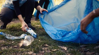 Geri dönüşüm için çöp ve plastik atık toplayan aktivistlerden oluşan bir ekip çöp temizleme araçları ve çöp torbalarıyla ormanı temizliyor. Ormandan çöp toplayan insanlar, aktivizm. Kapatın. Kamera B.