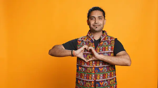 stock image Portrait of jolly friendly indian man doing heart symbol shape gesture with hands. Cheerful nurturing person showing love gesturing, isolated over studio background, camera B