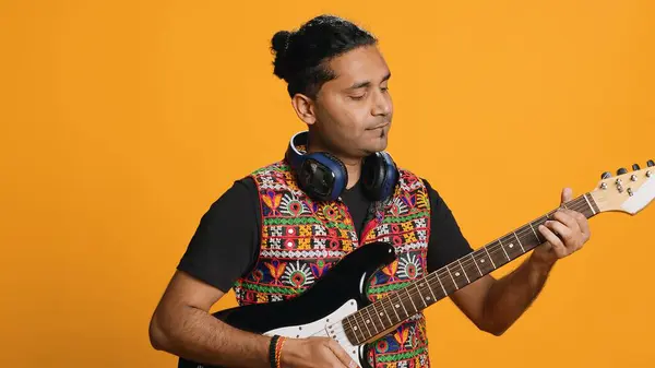 快乐的男人拿着电吉他 玩摇滚音乐 在工作室的背景上与世隔绝 快乐的印第安音乐家 用乐器 音乐会 相机A 免版税图库照片