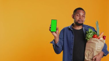 Stüdyoda yeşil ekran planlı akıllı bir telefon tutan genç bir yetişkin, bir kese kağıdında biyolojik bakkaliye taşıyor ve sağlıklı beslenme reklamları yapıyor. Vejetaryen kişi sunar. Kamera B.