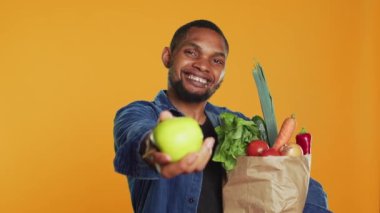 Afrika kökenli Amerikalı bir adam taze toplanmış yeşil bir elma sunuyor, kameranın önünde organik biyolojik meyveleri gösteriyor. Sağlıklı beslenmeyi ve vegan beslenmeyi savunan mutlu insan. Kamera A.