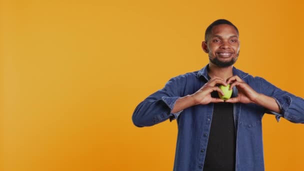 African American Relaxed Guy Does Heart Shape Sign Apple Recommending — Vídeos de Stock