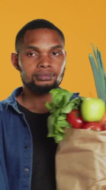 Dikey Video Genç yetişkin yanlışlıkla etik kaynaklı meyve ve sebzelerle dolu kağıt torbasından elma düşürüp çeşitli organik ev yapımı ürünler alıyor. Vejetaryen yaşam tarzını destekle. Kamera.