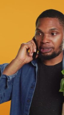 Dikey Videolu Genç Yetişkin, market alışverişi sırasında bir telefon görüşmesine cevap veriyor, bir kese dolusu çevre dostu ürün taşıyor ve akıllı telefondan konuşuyor. Yerel çiftçilik ilanları. Kamera.