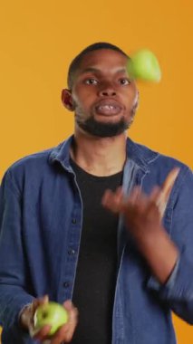 Stüdyoda olgun yeşil elmalarla hokkabazlık yapan dikey Video Oynayıcı, fırlatma ve yakalama ile sürekli hareket halinde tutuyor. Yetenekli adam organik meyvelerle eğleniyor.