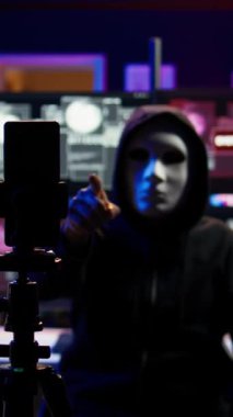 Gizli üste fidye videosu çeken bir hackerın kullandığı üç ayaklı telefondaki kameraya dikey video odaklan. Şantajı kaydetmek için maskeli siber suçlu tarafından kullanılan akıllı telefonu kapat
