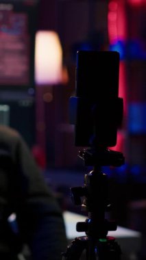 Gizli üste fidye videosu çeken bir hackerın kullandığı üç ayaklı telefondaki kameraya dikey video odaklan. Şantajı kaydetmek için maskeli siber suçlu tarafından kullanılan akıllı telefonu kapat