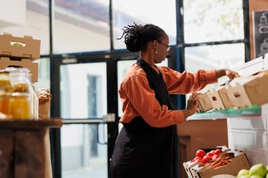 Afro-Amerikalı bir mağaza. Taze ürünleri, plastiksiz ambalajları ve toplu ürünleri olan bir çevre dostu mağaza. Zenci kadın raflarda sebze ve meyve yetiştiren çiftliklerle dolu kutular hazırlıyor.