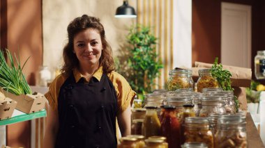 Gülümseyen sıfır atık süpermarket sahibinin portresi, iklim etkisini azaltmak için kirletici olmayan cam kaplar kullanıyor. Yerel bakkal dükkanında ürünleri düzenleyen neşeli bir tüccar