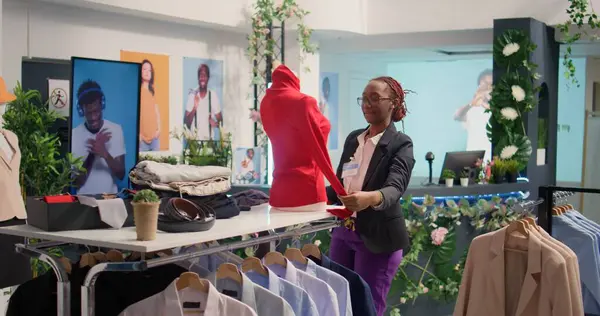 Meticulous retail assistant working in luxury fashion boutique, putting on women blouse on mannequin. Experienced african american employee showcasing new collection of trendy garments