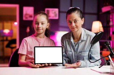 Sevimli kız ve annesi onun online içeriğini izleyen çocuklar arasında popüler olan boks modelleme tabletini çekiyorlar. Neşeli kız ve anne izole ekran cihazını açan video kaydediyor