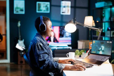 Afro-Amerikalı kadın laptopta rekabetçi video oyunu oynuyor. Siyahi kadın tamamen olaya dalmış, kulaklık takıyor ve oyun deneyimini geliştirmek için cihaz ekranı kullanıyor..
