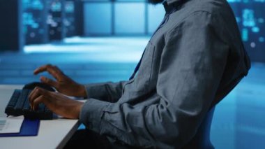 Sunucu merkezinde çalışan Afrikalı Amerikalı bir adam büyük miktarda veri işleme kapasitesine sahip. Klavyeye yazı yazan bilgisayar programcısı, ağ kaynaklarını kontrol eden sunucuları güncelliyor, görüntüyü kapat