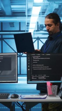 Dikey video Orta Doğulu yönetici sunucu merkezindeki işyerinde elektronik ve çok ırklı işçiler üzerinde inceleme yapıyor. Takım lideri dizüstü bilgisayardaki evrakları okuyor, altyapı belgelerini doğruluyor