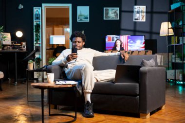 Kanepede uzanmış arkadaşlarıyla telefonda sohbet ediyor, rahat oturma odasında eğleniyor. Adam rahat koltukta rahatlıyor, sosyal medya yayınında kayıyor, ilginç gönderiler karşısında hayrete düşüyor.