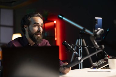 ASMR içerik yaratıcısı selfie çubuğunda kaliteli mikrofon ve cep telefonu kullanarak stres karşıtı videolar ve fısıltı sesleri yapıyor. Profesyonel mikrofon ve telefon kamerasıyla meditasyon Zen içeriğini çeken bir adam.