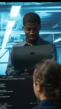 Veritabanı 'ndaki gülümseyen Afrikalı Amerikalı müdür devre dışı kalmamak için elektronik eşyaları kontrol ediyor. Ekip lideri, sunucu odasının altyapı bileşenlerindeki çalışanları denetleyen bir dizüstü bilgisayar tutuyor.