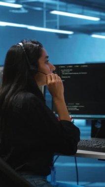 Bilgi işlem destek uzmanlarından oluşan dikey video ekibi bilgisayar ağı güvenlik veri merkezinde sunucu sıralarını denetleyerek birlikte çalışıyor. Meslektaşlarının yanındaki kadın denetleme yaparken mikrofonla konuşuyor.